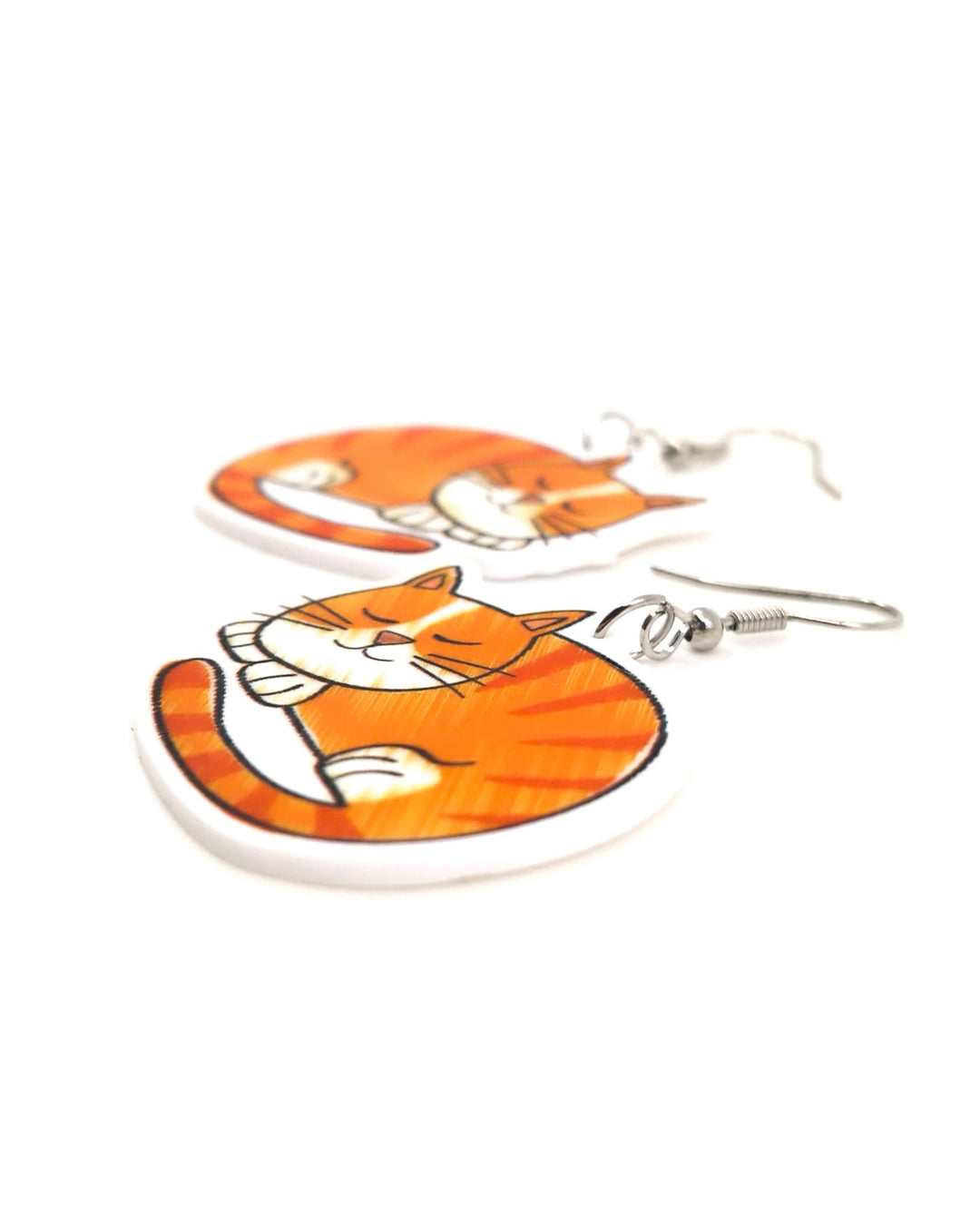 Close-up angled view of large ginger cat drop earrings with sleeping orange tabby acrylic charms and silver hooks.