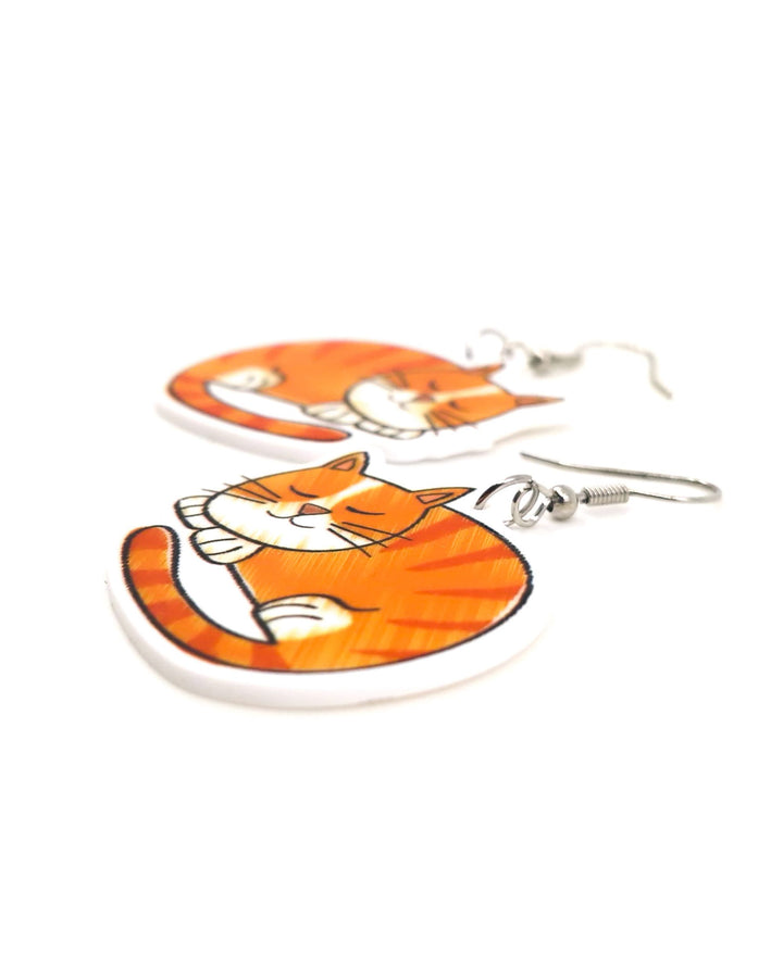 Close-up angled view of large ginger cat drop earrings with sleeping orange tabby acrylic charms and silver hooks.