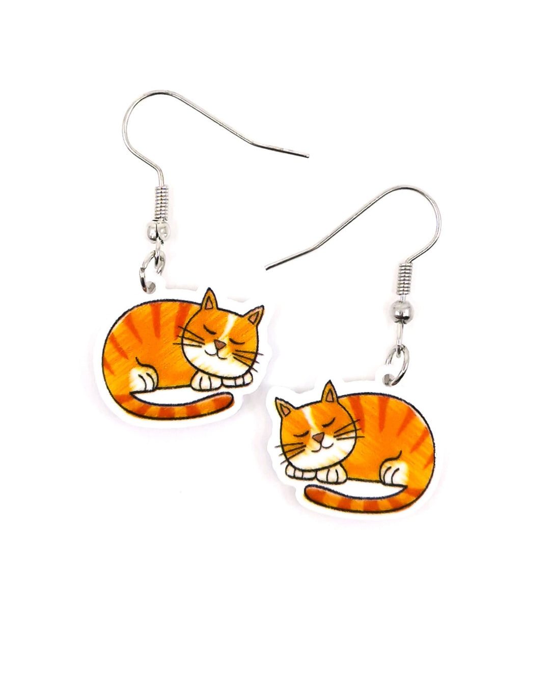 Close-up of medium ginger cat drop earrings with sleeping orange tabby acrylic charms and silver hooks on a light background.