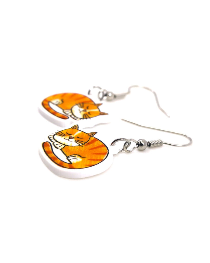 Pair of medium ginger cat drop earrings with sleeping orange tabby acrylic charms and silver hooks on a light background.