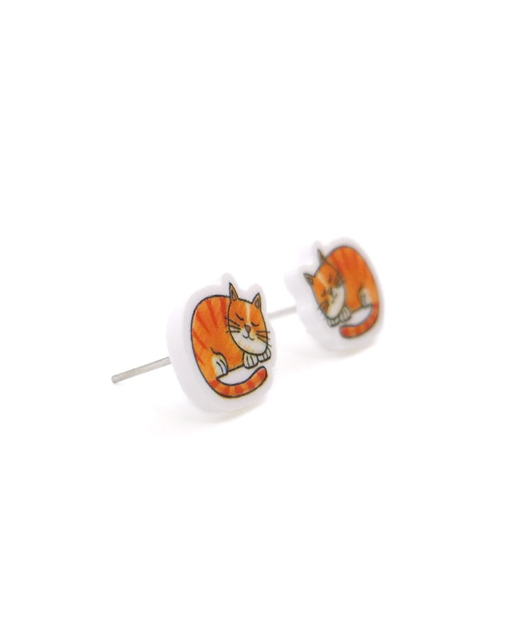 Close-up angled view of ginger cat stud earrings with sleeping orange tabby acrylic charms and silver posts.