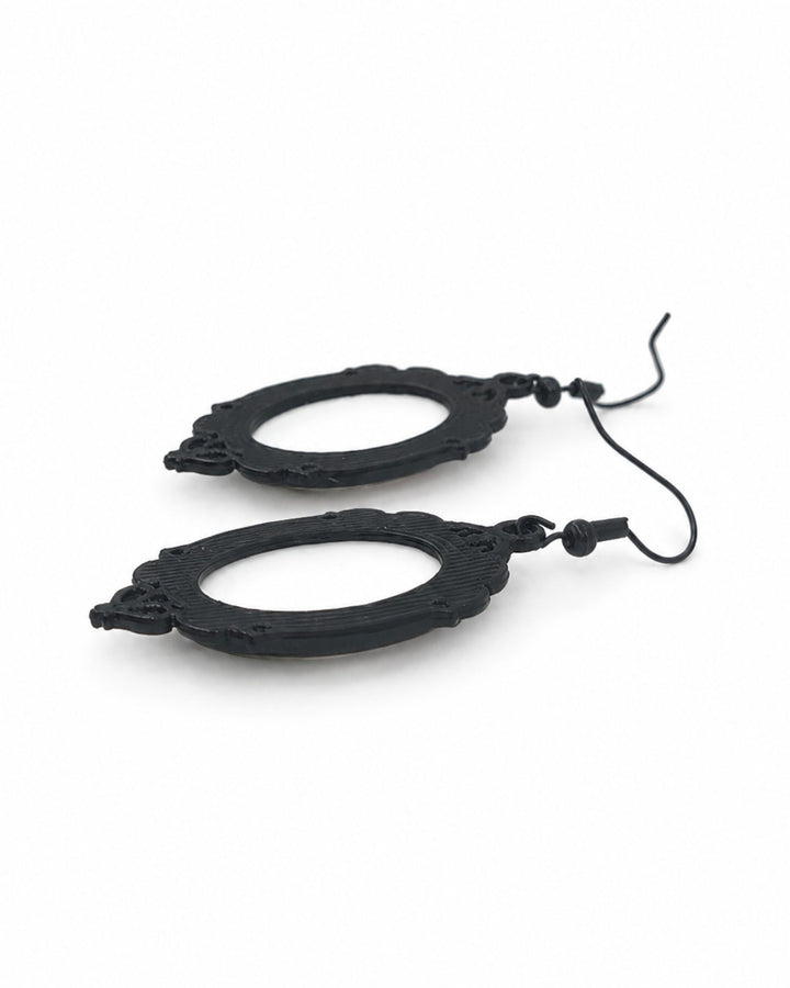 Close up of the back of Gothic skeleton cameo Halloween earrings with black ornate frames and black hooks, laid flat on white