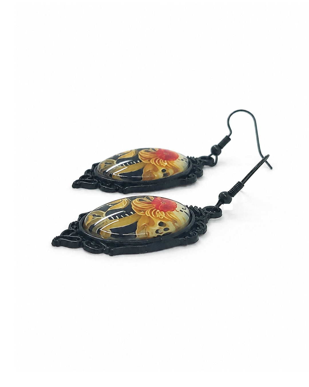 Close up of Gothic skeleton cameo Halloween earrings with black ornate frames, domed portrait charms, red rose details and black hooks, laid flat on white