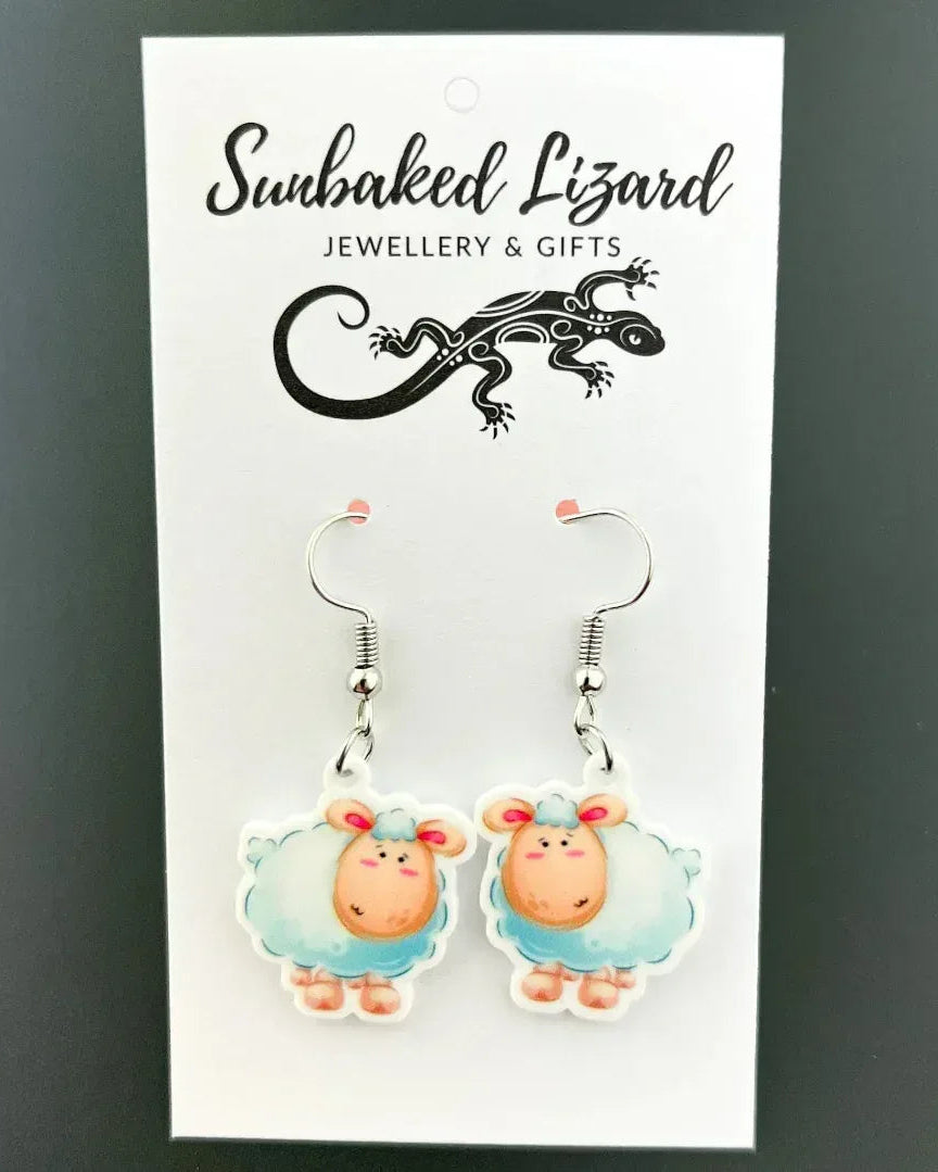 Lambie the Lamb drop earrings, two fluffy cartoon lambs with rosy cheeks on silver hooks on a Sunbaked Lizard backing card
