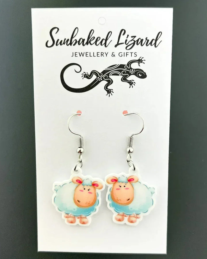 Lambie the Lamb drop earrings, two fluffy cartoon lambs with rosy cheeks on silver hooks on a Sunbaked Lizard backing card