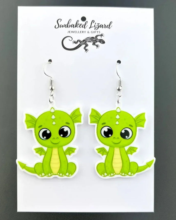 Maisy the Baby Dragon drop earrings, two lime green cartoon dragons with big eyes on silver hooks on a Sunbaked Lizard backing card
