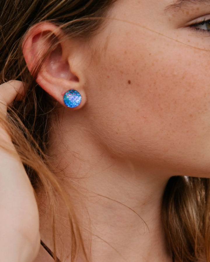 Blue mermaid scale stud earrings worn on ear