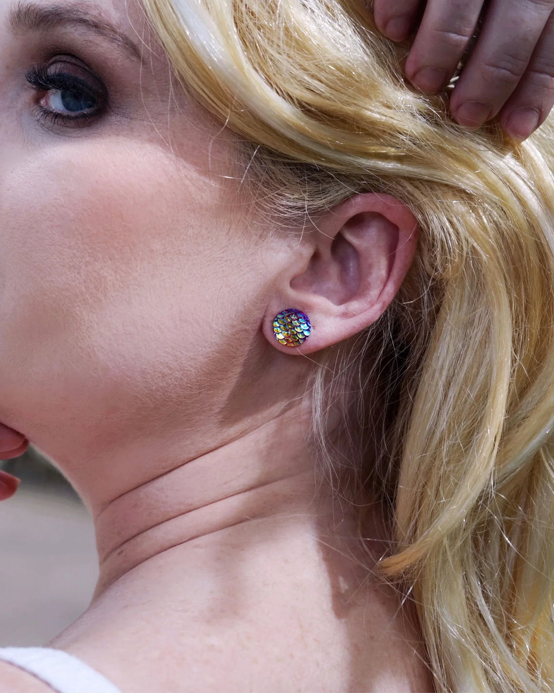 Side view of a woman with blonde hair and colorful mermaid glitter earrings, outdoors.
