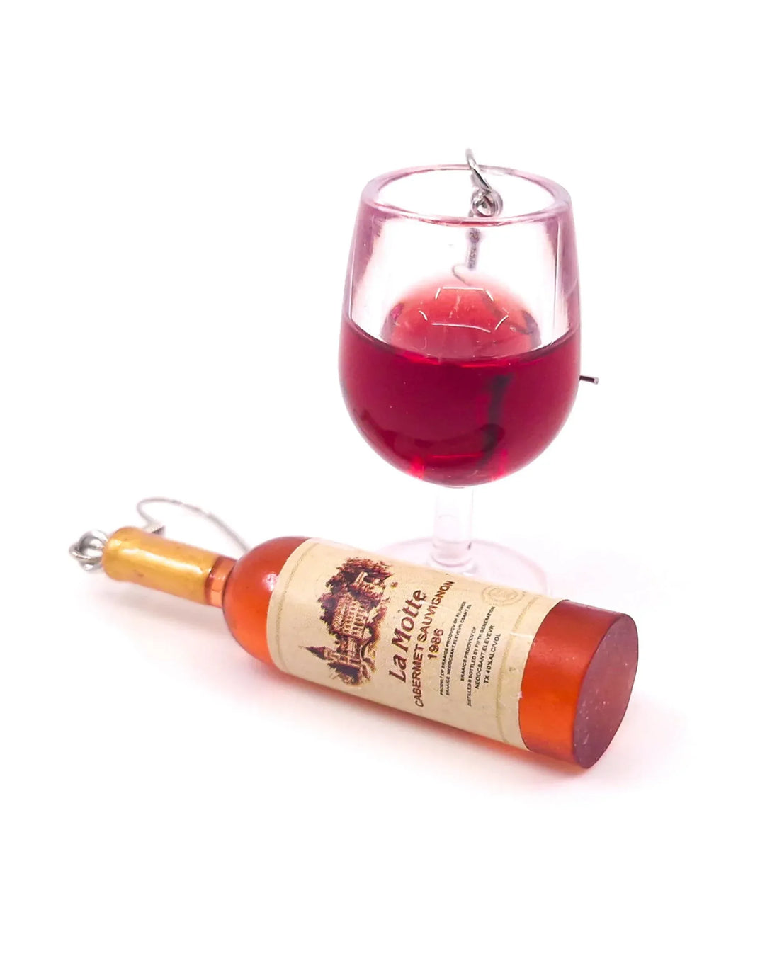 Close-up of miniature red wine bottle and wine glass novelty earrings with realistic detailing.
