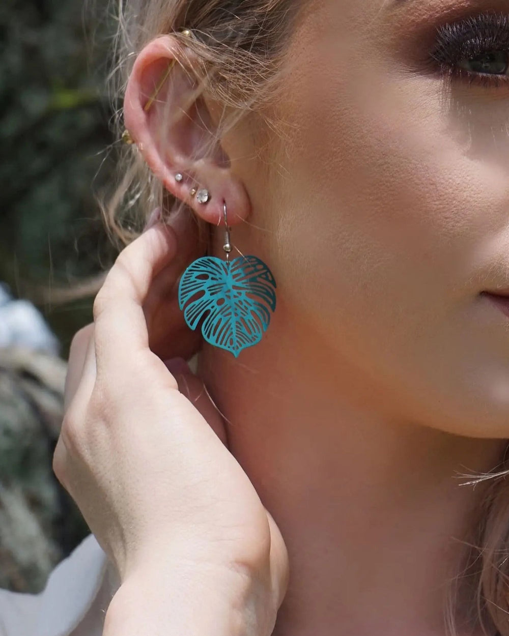Woman wearing teal monstera leaf drop earrings by Sunbaked Lizard