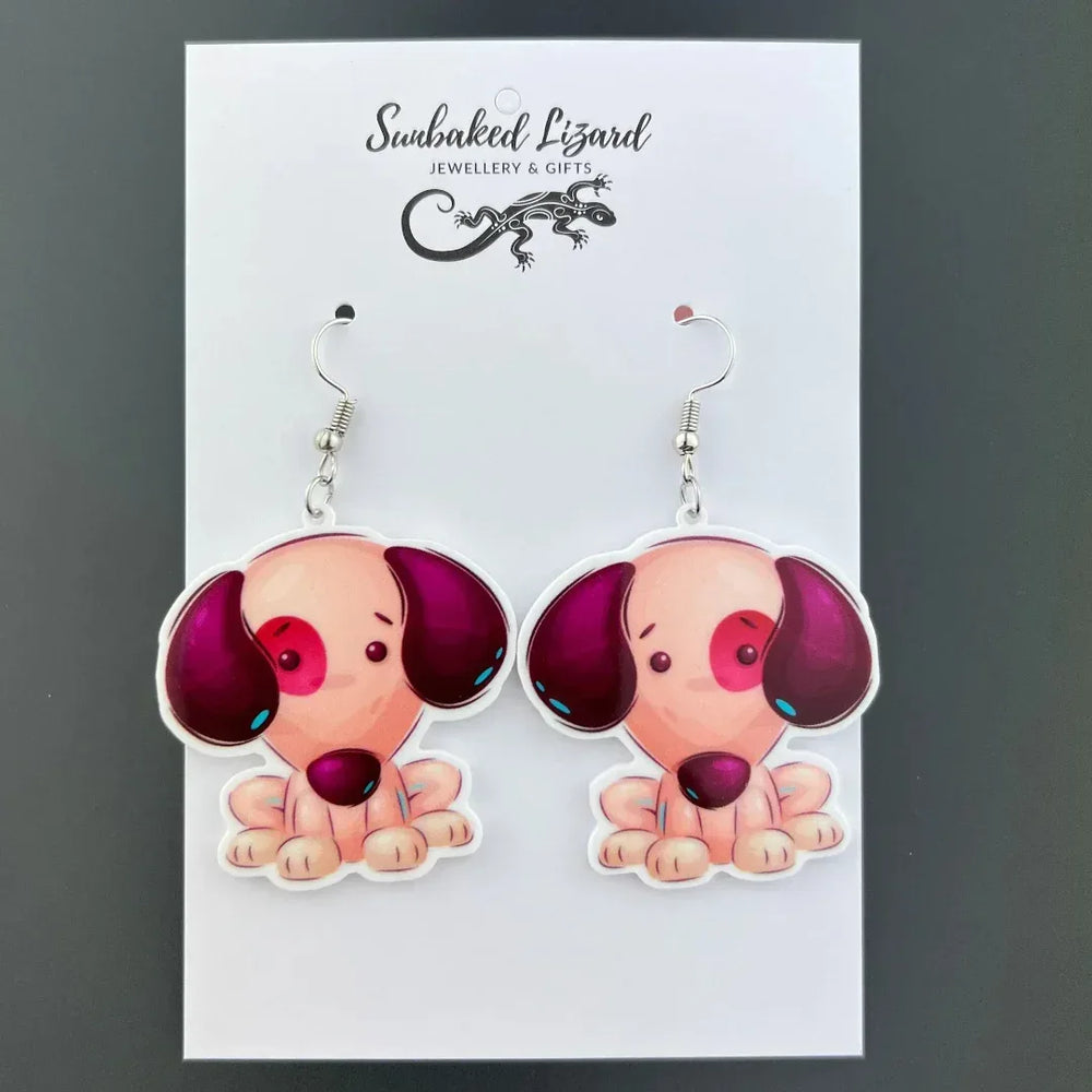 Patch the Puppy drop earrings, seated puppy acrylic charm with mismatched ears on silver hooks on a Sunbaked Lizard backing card