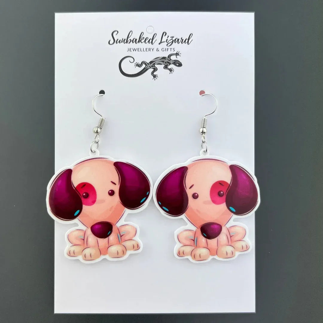 Patch the Puppy drop earrings, seated puppy acrylic charm with mismatched ears on silver hooks on a Sunbaked Lizard backing card