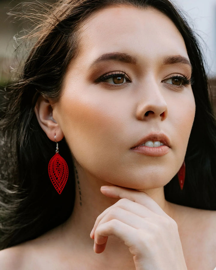 Model wearing red botanical leaf dangle earrings showing length and filigree-style cut-out detail