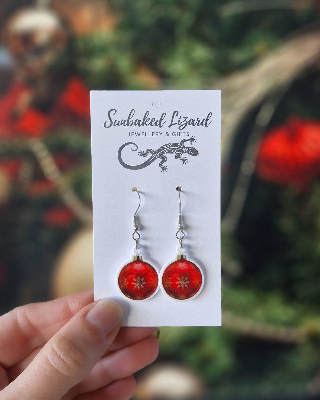 Red Christmas bauble earrings with gold snowflakes on a glossy acrylic charm, hanging from silver hooks n a Sunbaked Lizard backing card to show scale