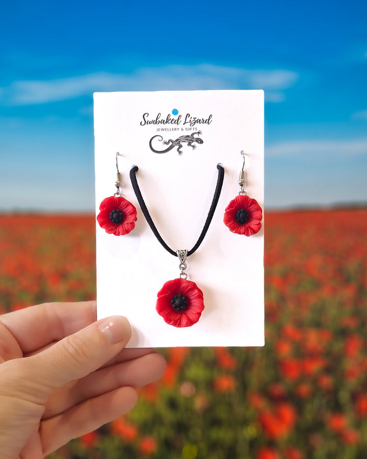 Red poppy necklace and matching drop earrings set on Sunbaked Lizard card with poppy field background