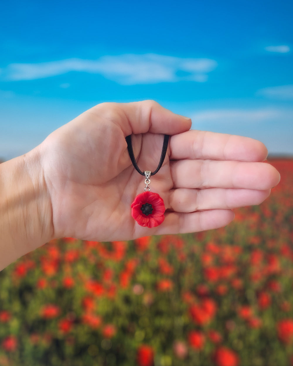 Red poppy necklace held in front of a poppy field background
