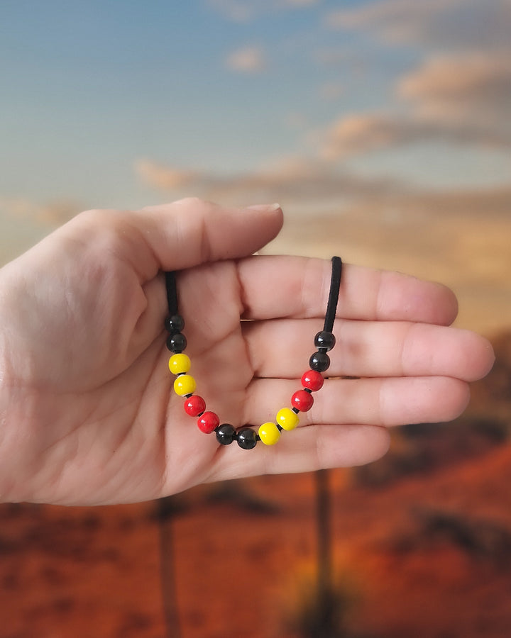 Red, yellow and black Indigenous inspired necklace held in front of warm landscape background