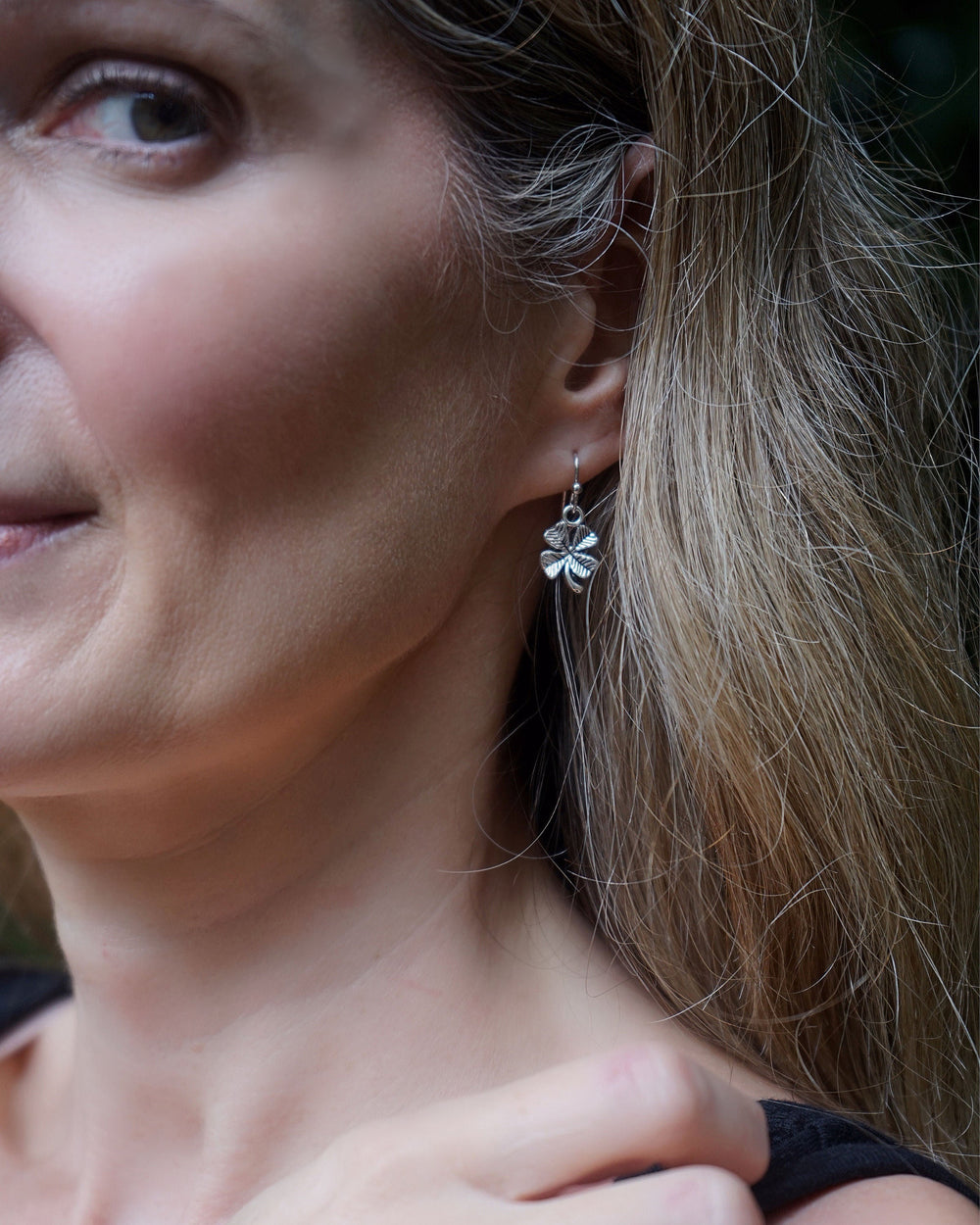 Close-up of a model wearing silver-tone Shamrock Four Leaf Clover Charm Earrings with a textured lucky clover design.