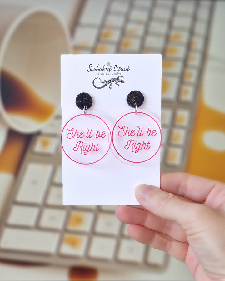 She’ll Be Right pink acrylic statement earrings displayed on a Sunbaked Lizard card with coffee spilled into a keyboard behind.