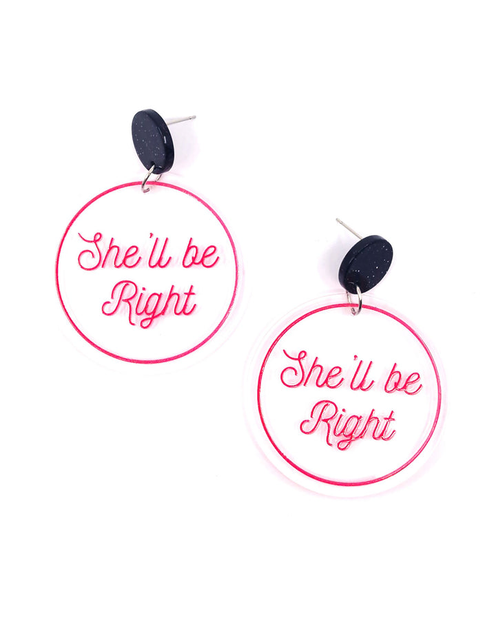 She’ll Be Right acrylic statement earrings with pink script on clear round drops and glitter black studs.