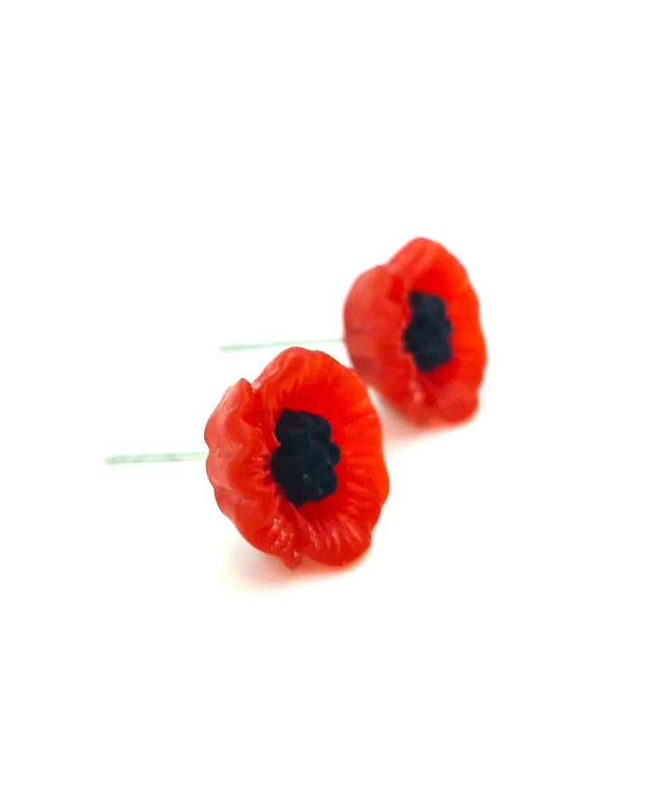 Side view of two red poppy earrings with black centers on a white background