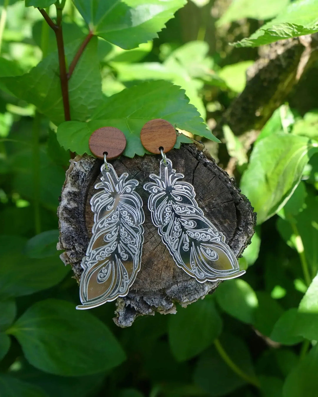 Silver shimmer feather dangle earrings with timber stud top displayed on tree trunk