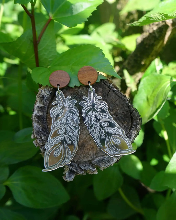 Silver shimmer feather dangle earrings with timber stud top displayed on tree trunk