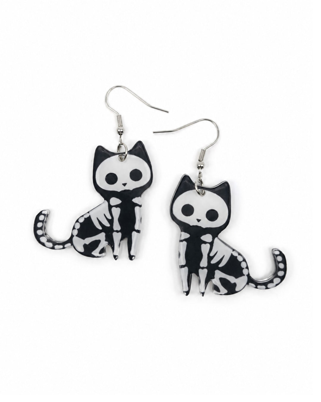 Halloween cat earrings with black and white skeleton kitty charms, curled tails and silver hooks on a white background