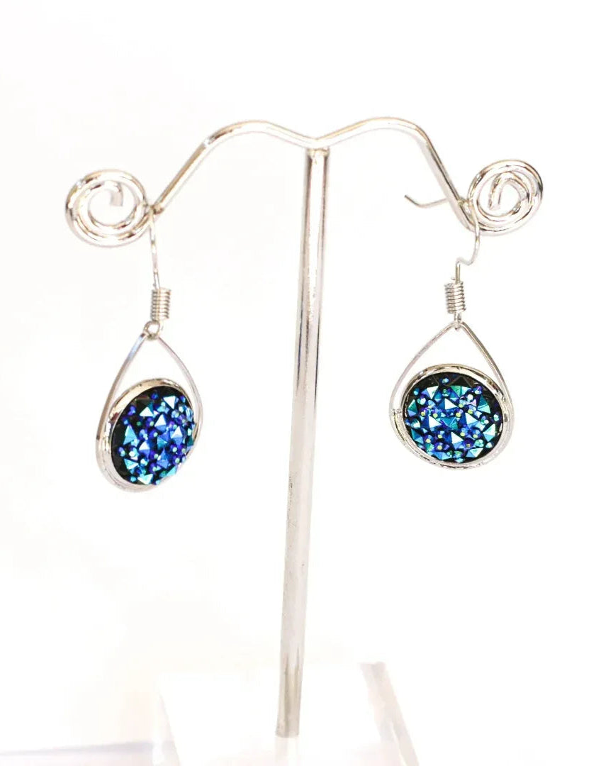 Dark blue sparkly teardrop earrings hanging on a silver earring stand