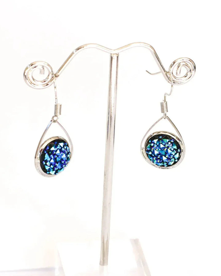 Dark blue sparkly teardrop earrings hanging on a silver earring stand