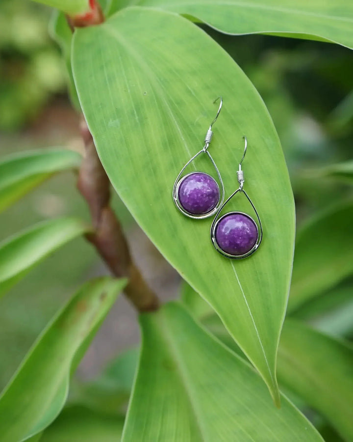 Purple stone teardrop earrings resting on a large green leaf in natural light