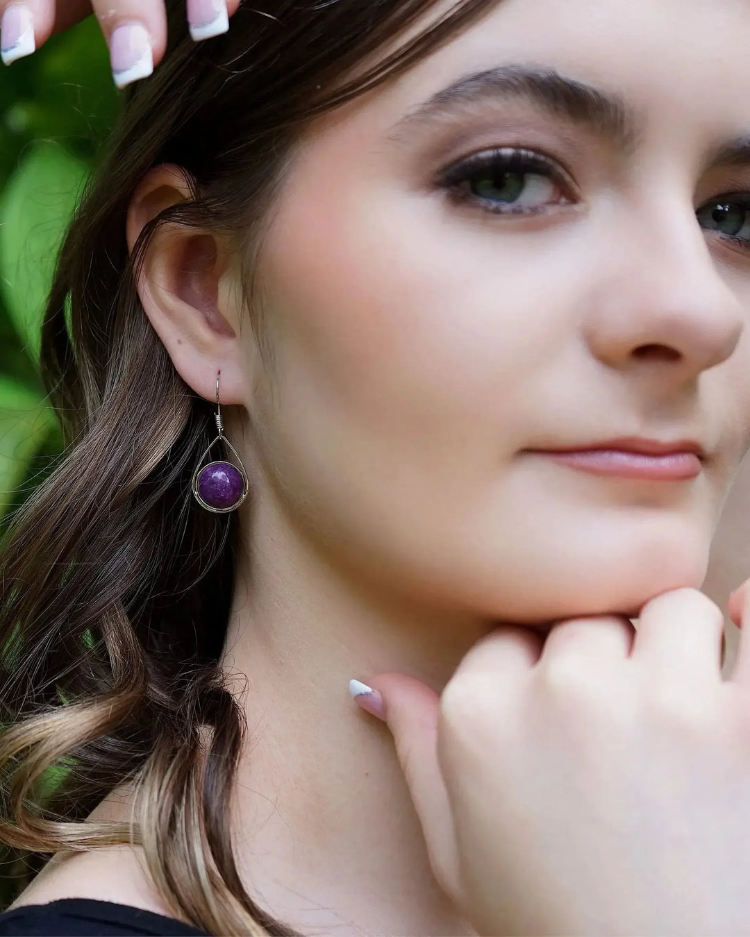 Close view of a purple stone teardrop earring hanging just below the ear lobe