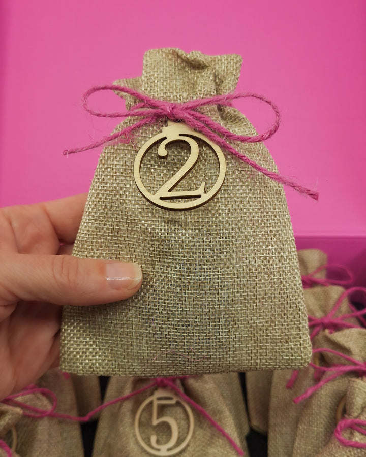 Open Sunbaked Lizard 12 Day Jewellery Advent Calendar with a hand holding one of the numbered burlap gift bags showing scale.