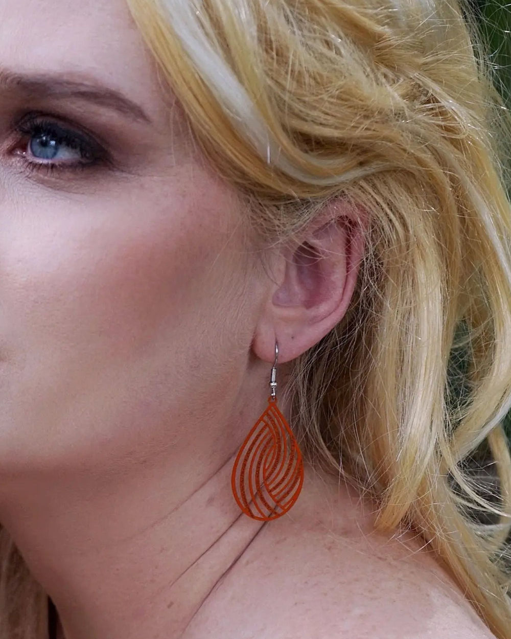 Side profile of model wearing orange swirl cut-out teardrop dangle earrings showing length and lightweight shape