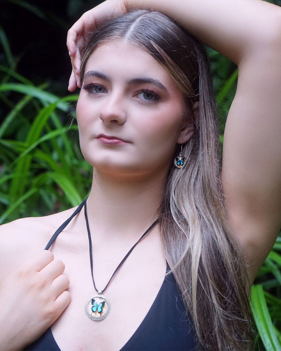 Model wearing Ulysses butterfly necklace and matching blue butterfly earrings in a leafy garden setting