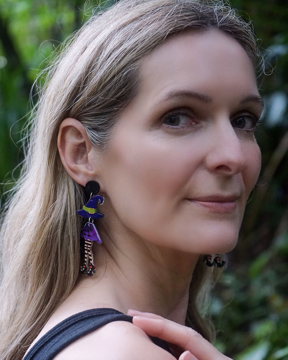 Model wearing Witch Stud Drop Earrings, a playful Halloween acrylic earring design with witch legs and pointed hats.