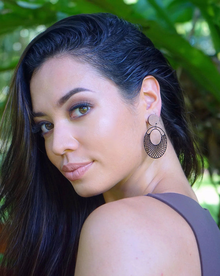 Model wearing black filigree round earrings with timber stud top and cut-out lattice circle drop, showing size and movement