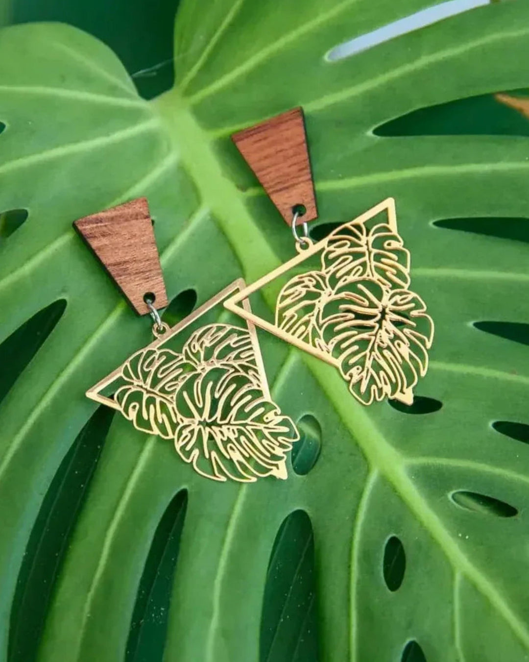 Timber and metal monstera leaf statement earrings sitting on a monstera left