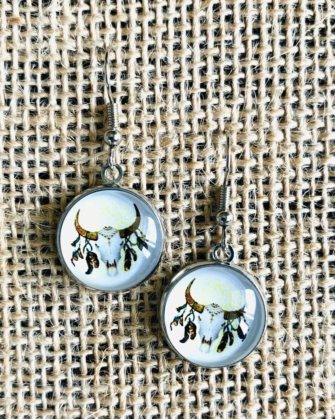 Close-up of round bull skull drop earrings in silver setting on textured fabric