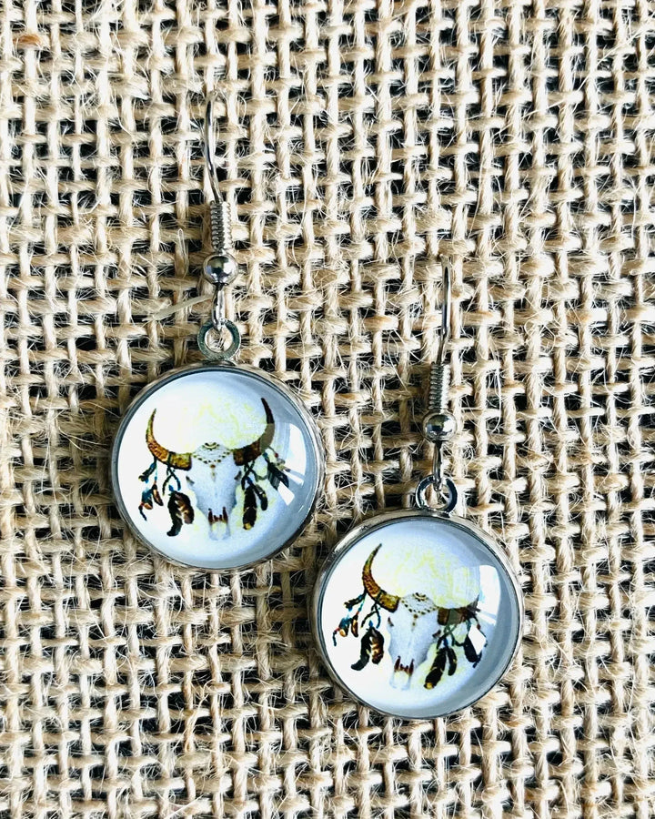Close-up of round bull skull drop earrings in silver setting on textured fabric