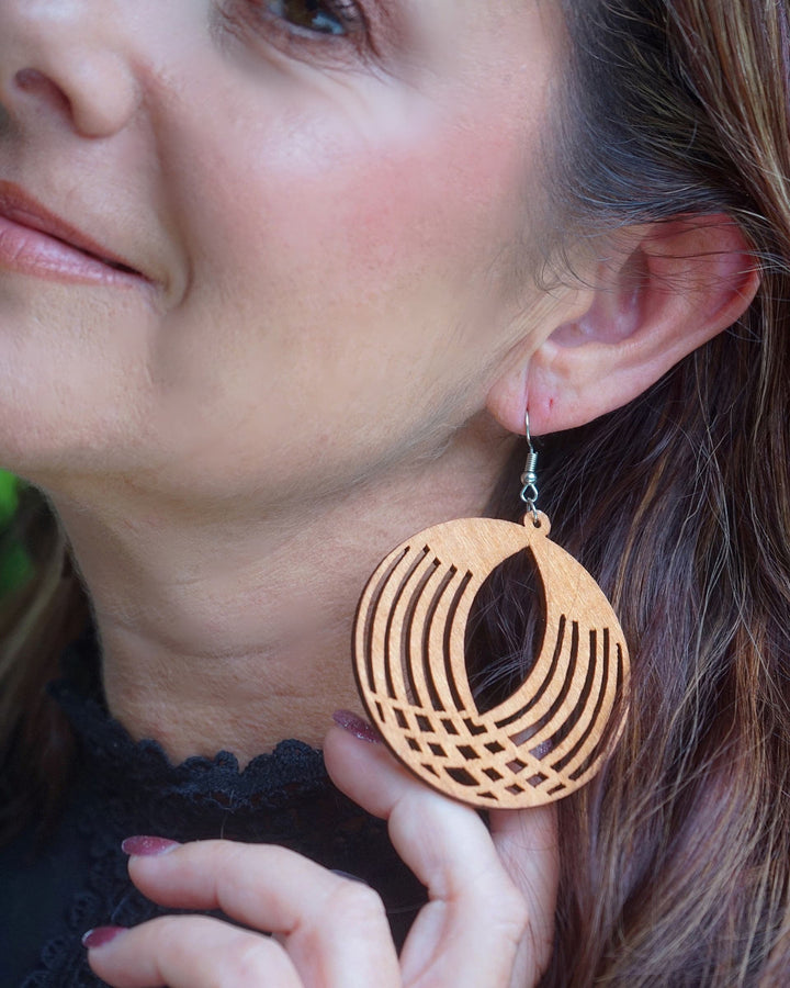 Model wearing large round geometrical timber drop earrings with cut-out pattern