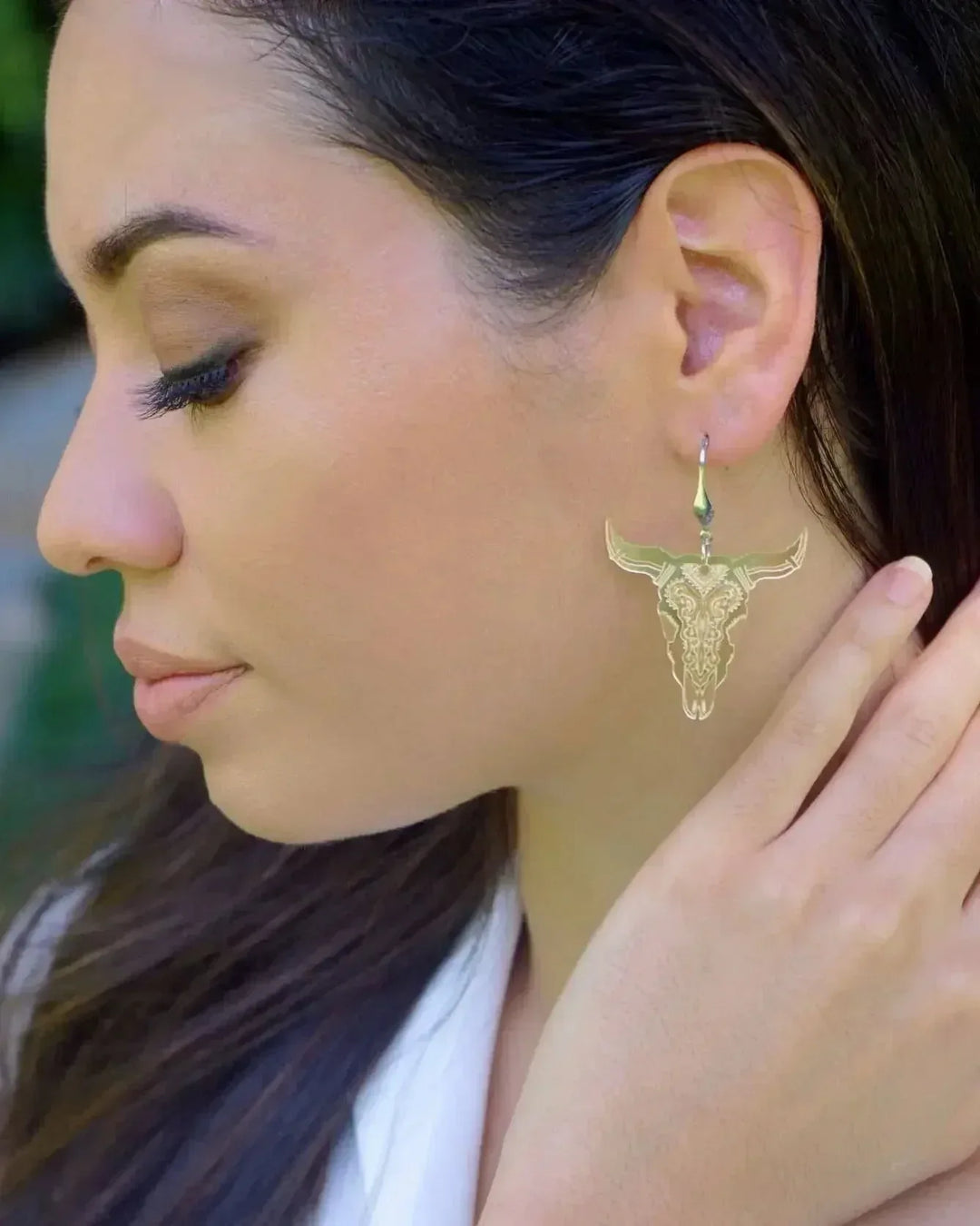 Woman wearing shimmer gold bull head dangle earrings with detailed filigree western skull design.
