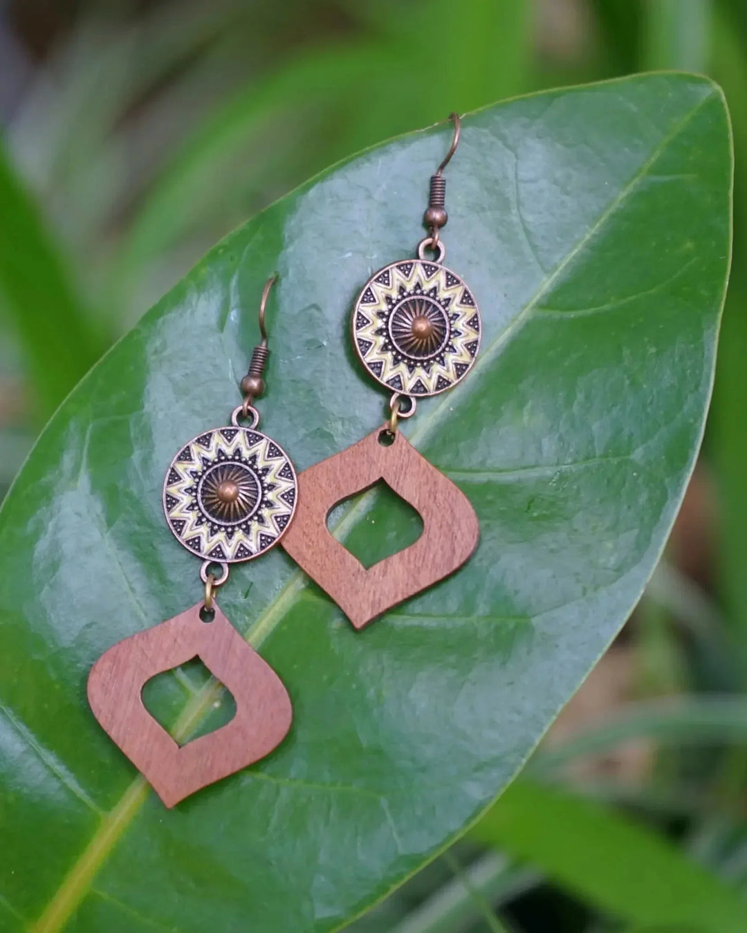Timber and copper sun drop earrings resting on a large green leaf