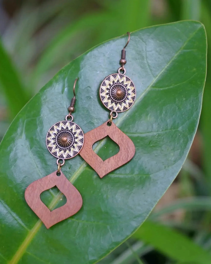 Timber and copper sun drop earrings resting on a large green leaf