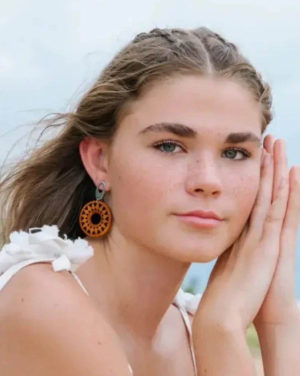 Model wearing timber sun pendant drop earrings at the beach for a natural coastal look.