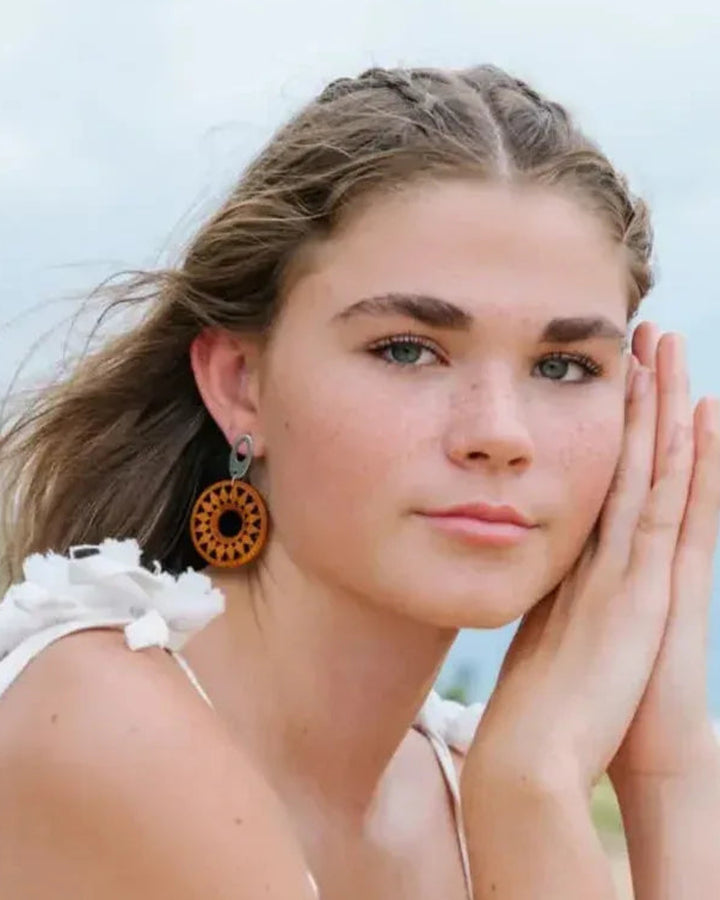 Model wearing timber sun pendant drop earrings at the beach for a natural coastal look.