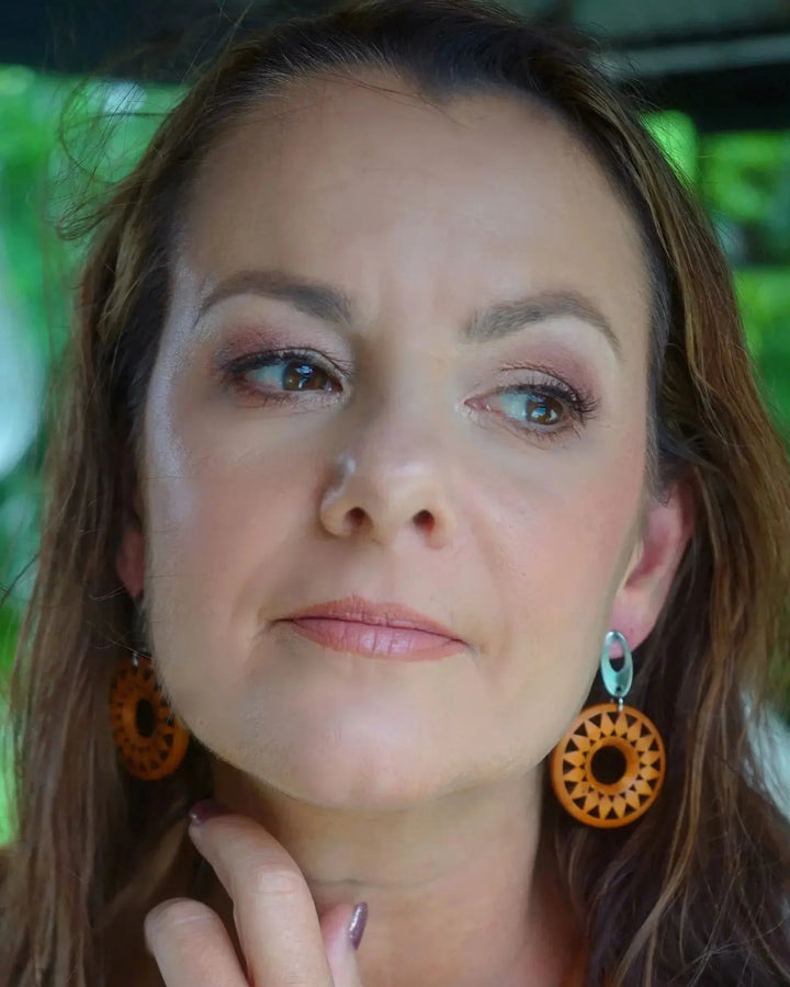 Timber sun pendant drop earrings with circular cut-out sunburst design and silver stud top on a model.