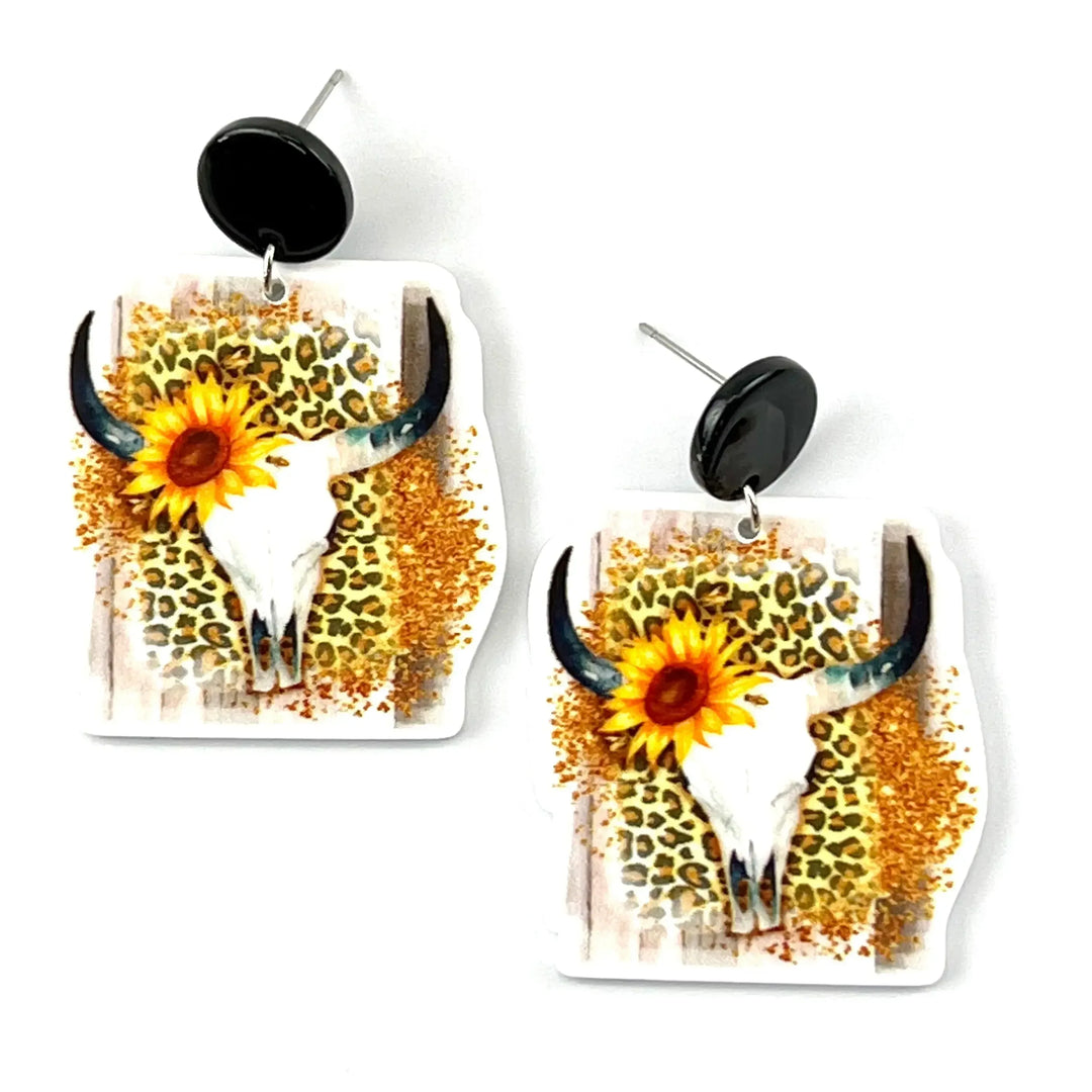 Western cow skull stud drop earrings with sunflower detail and leopard print background on white backdrop
