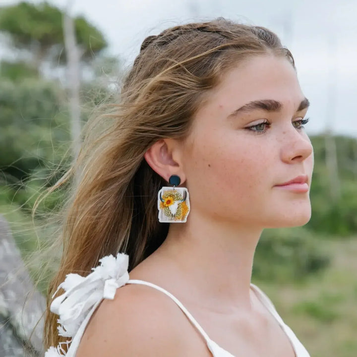 Side view of woman wearing western cow skull and sunflower leopard print statement earrings